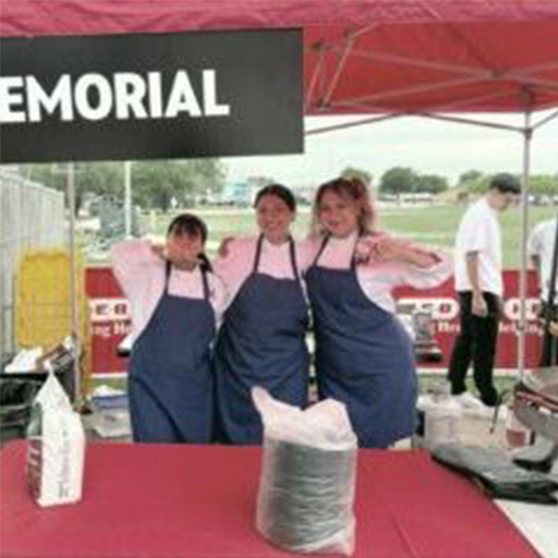 Penelope Medellin and two other people wearing aprons and standing under a tent