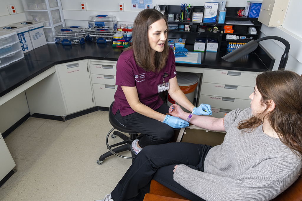 one woman sitting in chair while another woman sits next to her with blue rubber gloves on