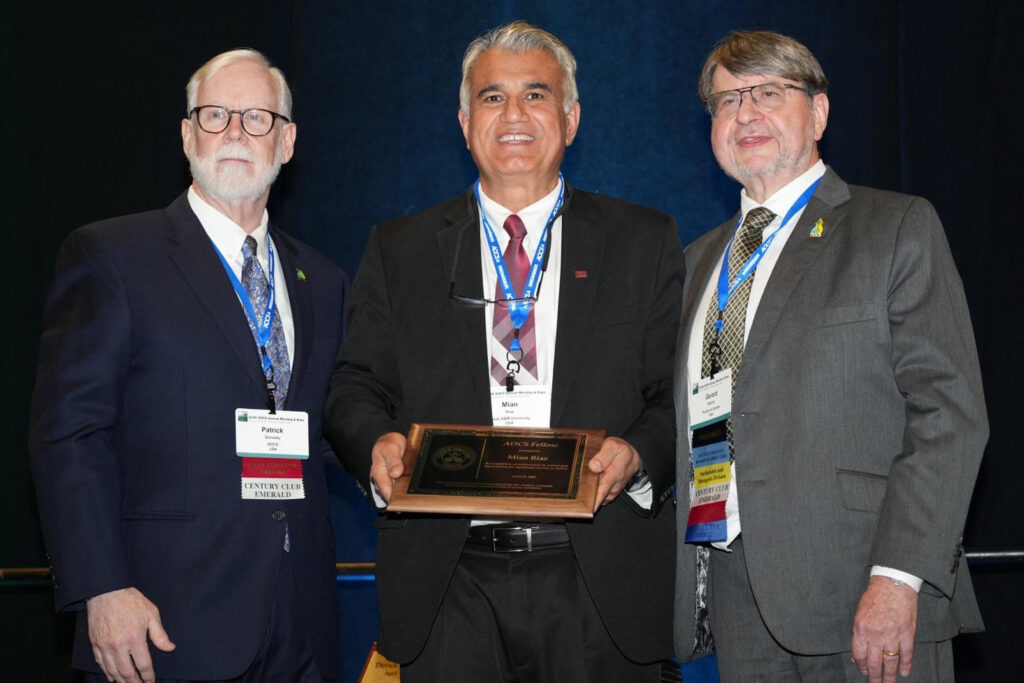 Mian Riaz stands between two men while holding his plaque he received for being named a Fellow by the American Oil Chemists’ Society