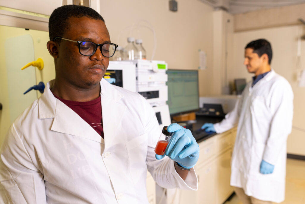 Student in lab inspecting a small vial of reddish substance