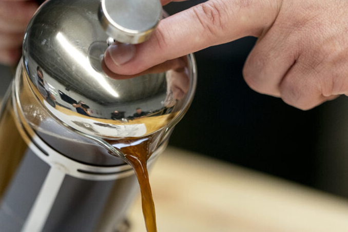 finger holding the lid on a canister while pouring coffee out
